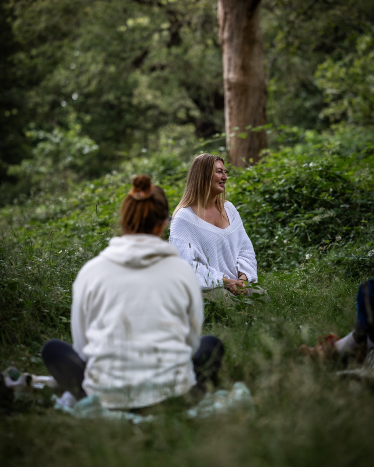 Linda in white guiding seated participants in green woodland