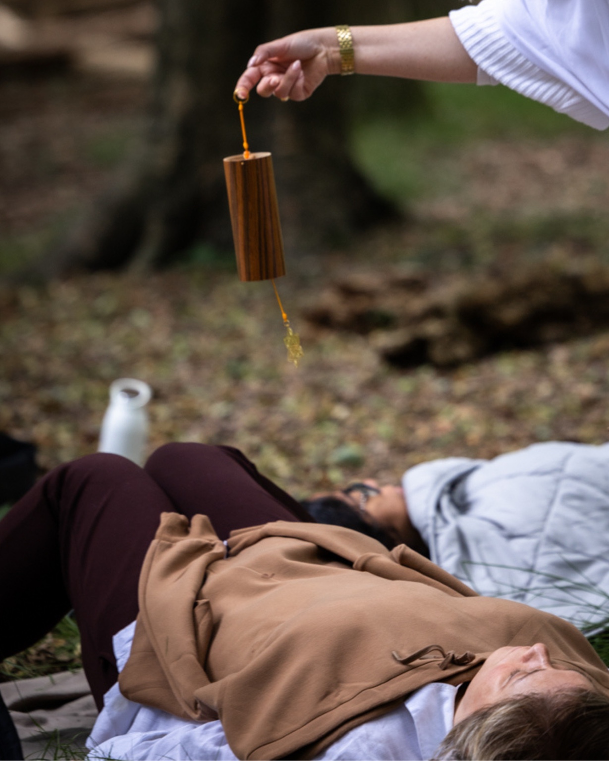 Linda playing a gentle chime while participants rest beneath the trees