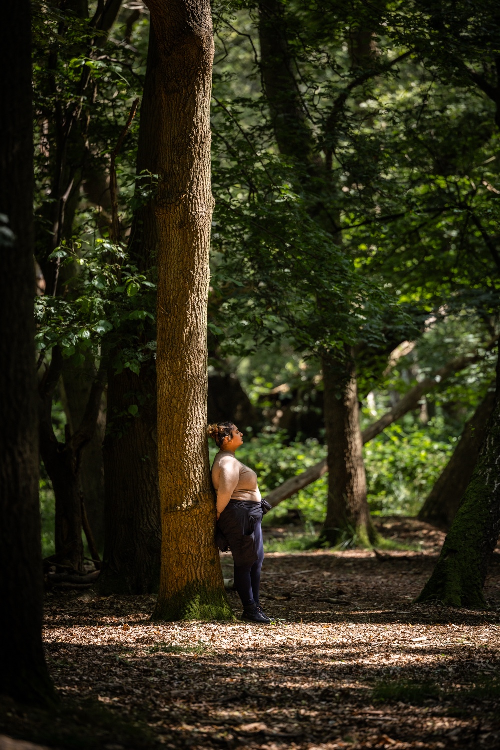 A woman pausing against a tree in the woodland
